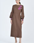 Woman wearing a brown dress with a floral embroidery on a white background