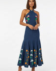 Model wearing embroidered Erva Dress a halter midi dress featuring tulip and jasmine embroidery on the bodice and flared skirt.