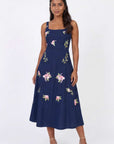 Model wearing the Fanm Mon Fisayo Dress with climbing rose embroidery, structured square neckline, and softly flared midi skirt against a neutral studio background.