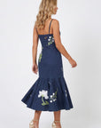 Model wearing the Fanm Mon Gayelle Dress with hand-placed floral embroidery, dragonfly details, adjustable straps, and flounced midi skirt shown from the back against a neutral background.