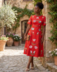 Model wearing the Fanm Mon Hannah Dress with tulip and poppy embroidery styled outdoors in a European-inspired courtyard, featuring a refined midi silhouette and artisan floral detailing