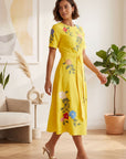 Model wearing Fanm Mon elegant embroidered Jess midi dress with floral blooms and green vine detailing and belted waist styled indoors for occasion and resort wear.