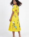 Back view of Fanm Mon Jess embroidered midi dress featuring floral botanical embroidery, short sleeves, flowing skirt, and tailored waist silhouette against off white background.