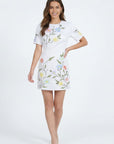 Model wearing the Fanm Mon Joe Dress in White featuring hand-placed wild poppy, cosmos, and buttercup embroidery on a tailored short sleeve mini silhouette against an off-white background.