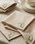 Napkins with Lily of the Valley Floral embroidery on a table setting with plates and glasses.