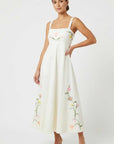Model wearing the Fanm Mon Leyla Dress featuring tulip, cosmos, buttercup, and lily embroidery, a square neckline, embroidered straps, empire waist, and flowing A-line silhouette.