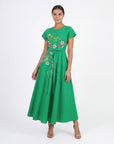 Model wearing the Fanm Mon Ritaj Dress featuring wildflower-inspired embroidery, cap sleeves, adjustable waist tie, and flowing full-length silhouette against a neutral studio background.