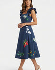 Woman wearing embroidered Tasya midi dress with ruffled shoulder straps and scattered jasmine, orchid, and tropical floral embroidery.