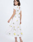 Back view of the Katrina Dress in white with yellow embroidered flowers, gathered skirt detailing, removable waist belt, and keyhole back closure.