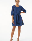 Model wearing the Fanm Mon Pearl Dress featuring a gathered round neckline, fabric-covered button front, three-quarter balloon sleeves, self-tie waist, tassel details, and floral embroidery.