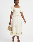 Model wearing the Fanm Mon Selma Dress showcasing the tailored square-neck bodice, peplum waist, embroidered floral detailing, and flowing tiered midi skirt.