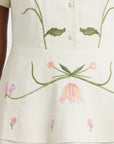 Close-up of the Fanm Mon Selma Dress highlighting the embroidered botanical motifs, decorative covered buttons, and intricate floral embroidery across the peplum waist.