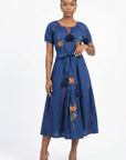 Model wearing the Fanm Mon Venya Dress featuring floral embroidery, short sleeves, tassel neckline, self-tie waist, and gathered midi skirt.