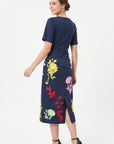 Back view of the Fanm Mon Blanka Dress in indigo blue showing the concealed center-back zipper, back slit, and multicolored floral embroidery extending around the skirt.