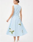 Back view of model wearing Fanm Mon Gemimi Dress in light blue showing the concealed center-back zipper, defined waist, and white floral embroidery along the flowing A-line midi skirt.