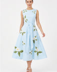 Model wearing Fanm Mon Gemimi Dress in light lagoon with a sleeveless round neckline, self-tie waist belt, and white botanical floral embroidery scattered across the full midi skirt.