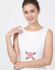 Close-up of model wearing Fanm Mon Hazel Dress in white, highlighting the softly rounded neckline, sleeveless bodice, and central pink rose embroidery with detailed green leaves at the waist.