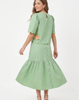 Back view of model wearing Fanm Mon Komarna Set in green showing scalloped detailing along the top, floral embroidery near the back hem, and a gathered midi skirt.