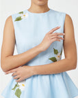 Close-up of Fanm Mon Malez Set in Light Lagoon highlighting the round neckline, tailored sleeveless bodice, gathered peplum, and white floral embroidery with yellow centers and green leaves.