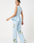 Back view of model wearing Fanm Mon Malez Set in Light Lagoon showing fabric-covered buttons along the fitted peplum top and scattered white floral embroidery on the wide-leg trousers