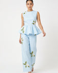 Model wearing Fanm Mon Malez Set in Light Lagoon featuring a sleeveless peplum top and wide-leg trousers with delicate white floral embroidery and green foliage