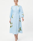 Model wearing the Fanm Mon Paysan Dress in light blue featuring white embroidered blossoms, fabric-covered buttons, and an A-line midi silhouette