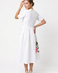 Back view of model wearing Fanm Mon Rumen Dress in white showing the concealed center-back zipper, fitted bodice, gathered waist, and flowing A-line midi skirt with pink floral embroidery along the side.