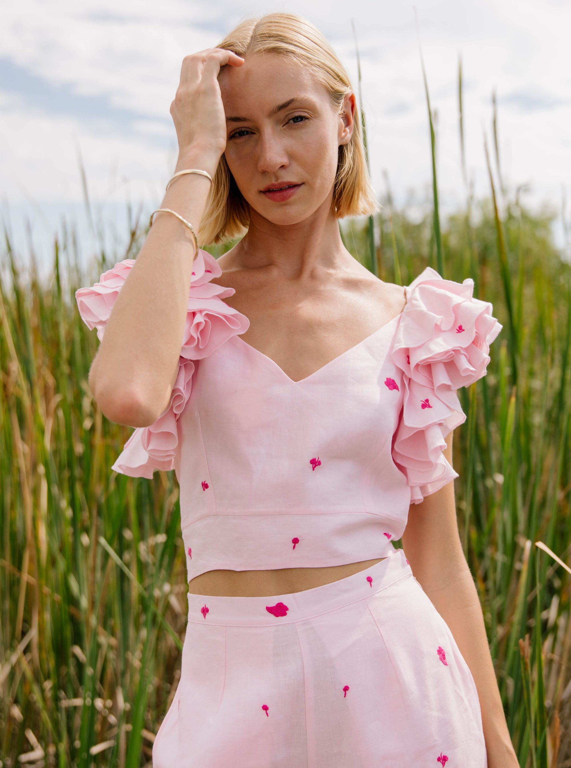 2 Piece Linen Top and Pants Set. Sleeveless top features ruffles with intricate embroidery detail and back detail of bow and button closure, while the wide-leg pants boast a matching embroidery detail and on-seam pockets for a cohesive look.