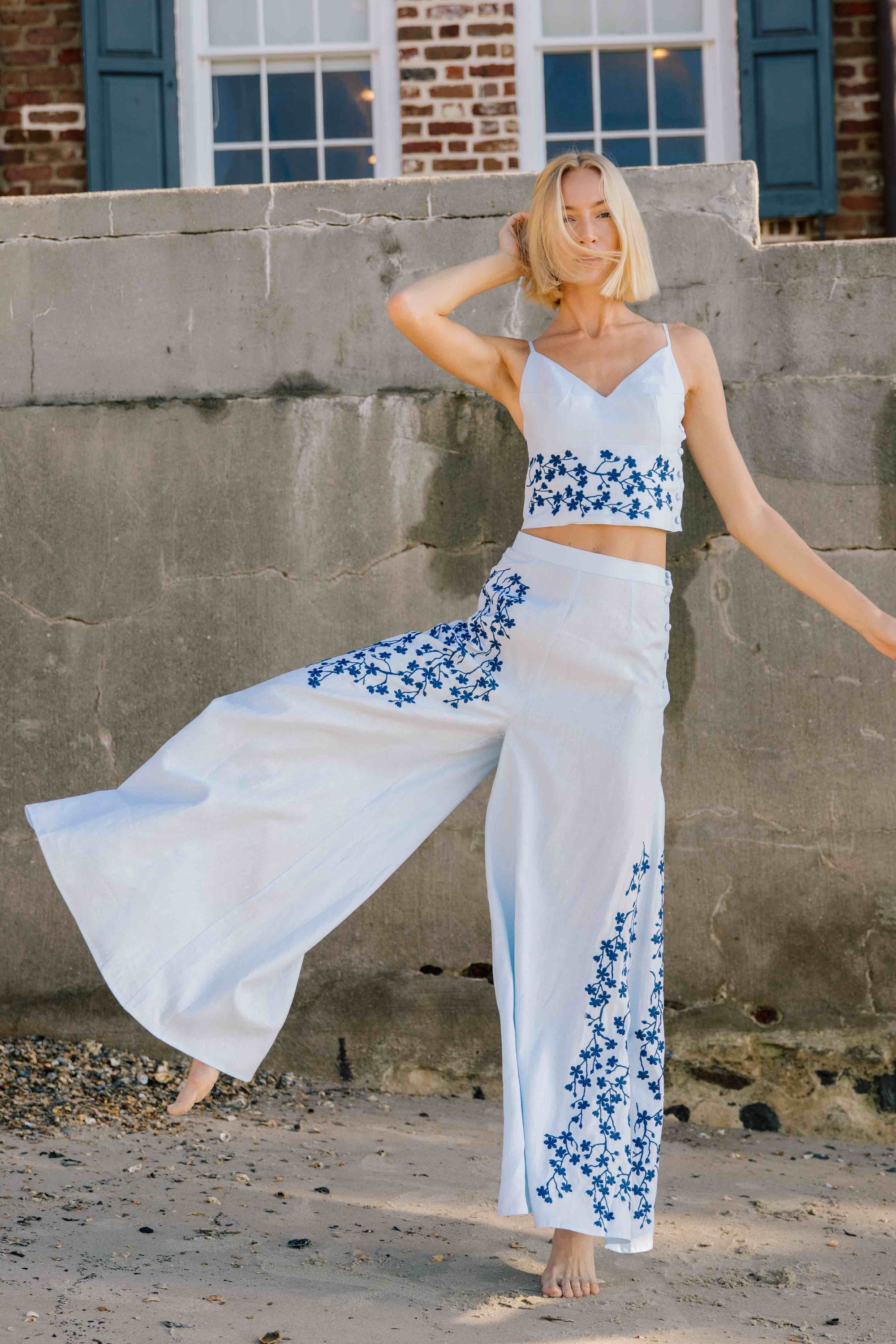 Fanm Mon Cali Pant Lifestyle Image. 2 Piece Linen Top and Pants Set. Top features intricate embroidery detail and a side button closure, while the wide-leg pants boast a matching embroidery detail and side button closure for a cohesive look.