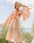 FANM MON DAYNA LINEN DRESS - LIFESTYLE IMAGE.Kimono Sleeve Knee Length Linen Dress. Featuring a biased cut, plunging neckline, embroidery detail on the front, and bow tie front detail.