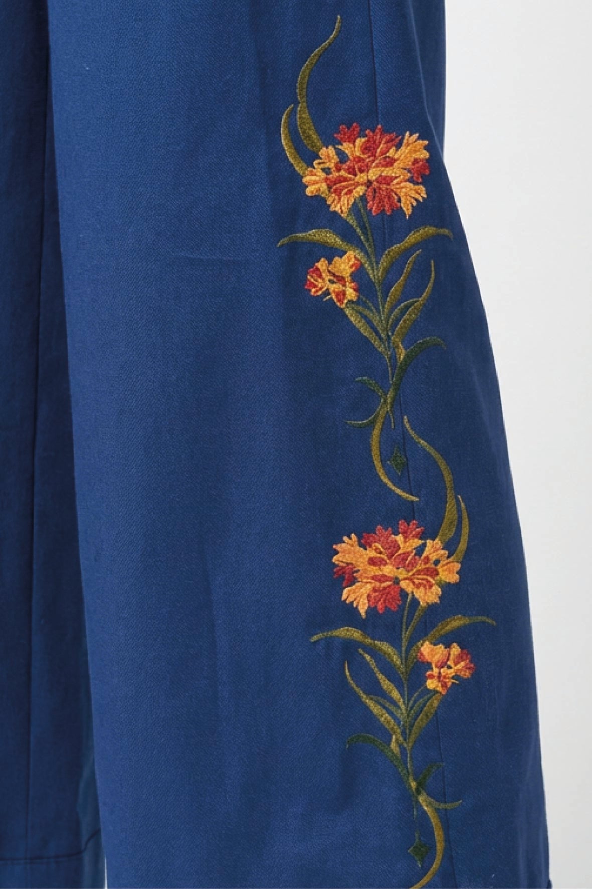 Fanm Mon Arel Pant detail featuring orange and red fire-inspired floral embroidery with green stems and leaves up the sides of the pants.