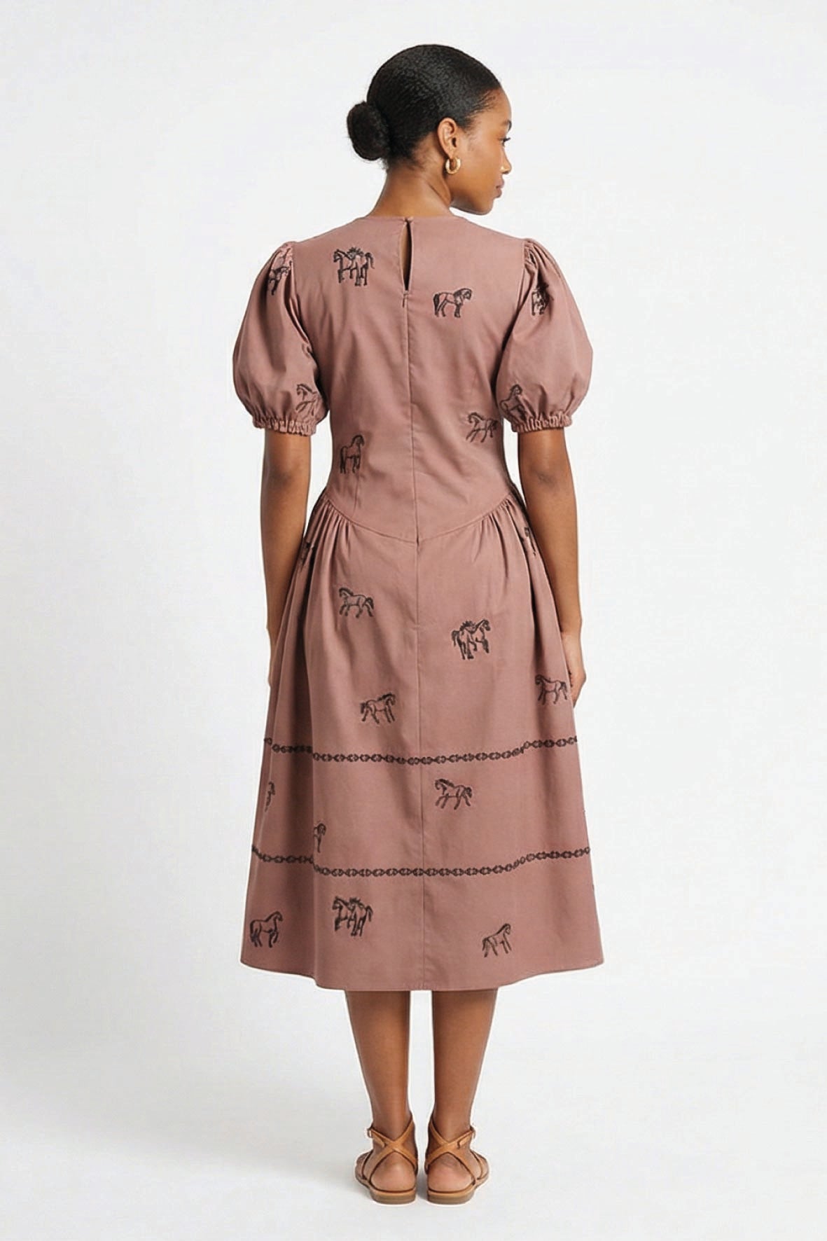 Back view of the Fanm Mon Aviva Dress featuring black horse embroidery, short puff sleeves, a drop waist, and embroidered bands along the full midi skirt.