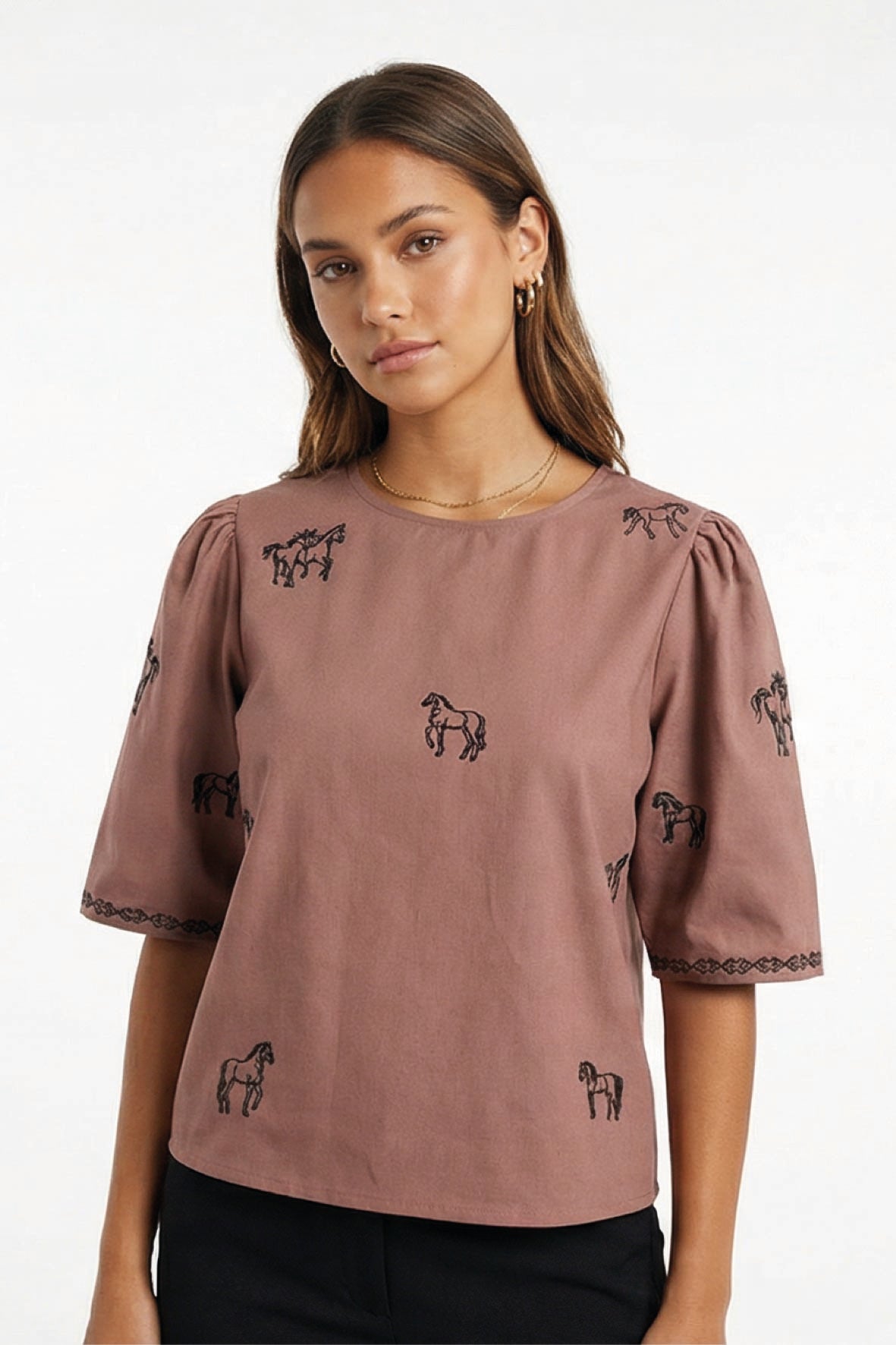 Model wearing Fanm Mon Cait short-sleeve blouse with black embroidered horse motifs, paired with black pants, against a plain white background.