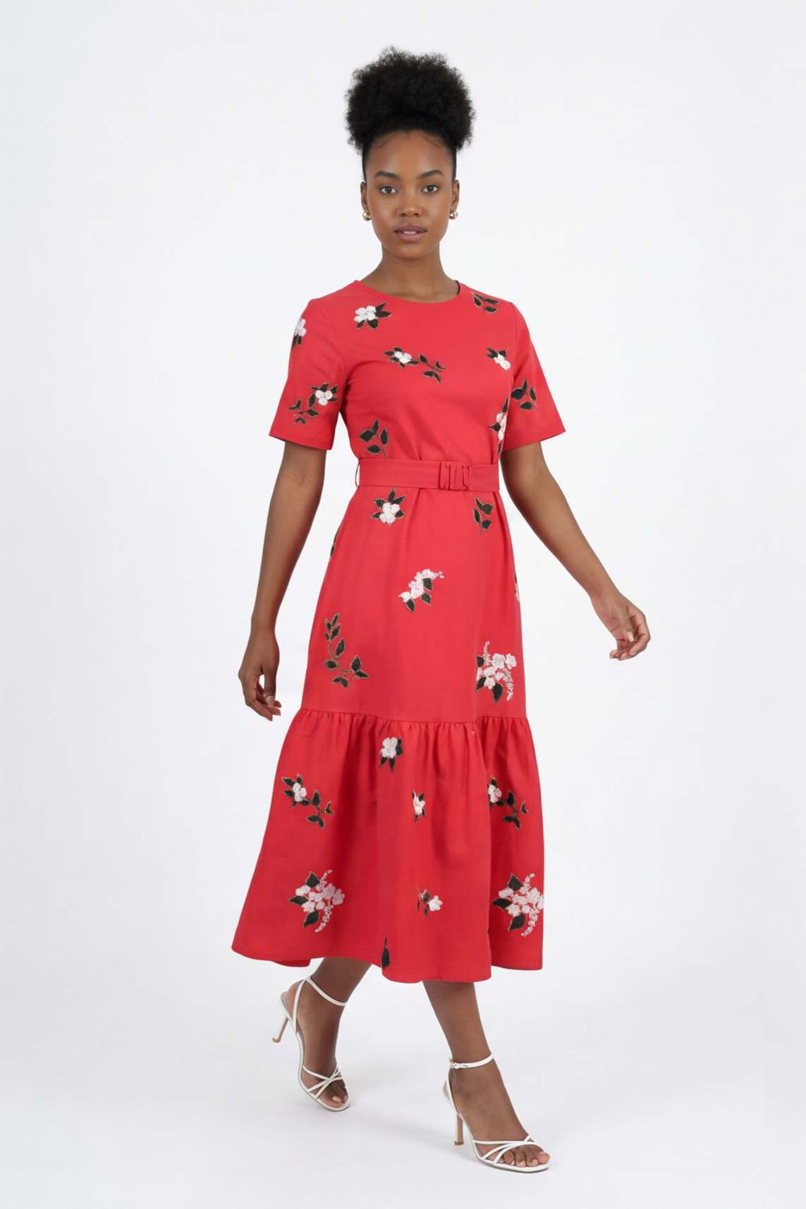 Model wearing the Liza Dress featuring jasmine-inspired floral embroidery, a buckle waist belt, short sleeves, and a gathered midi hem.