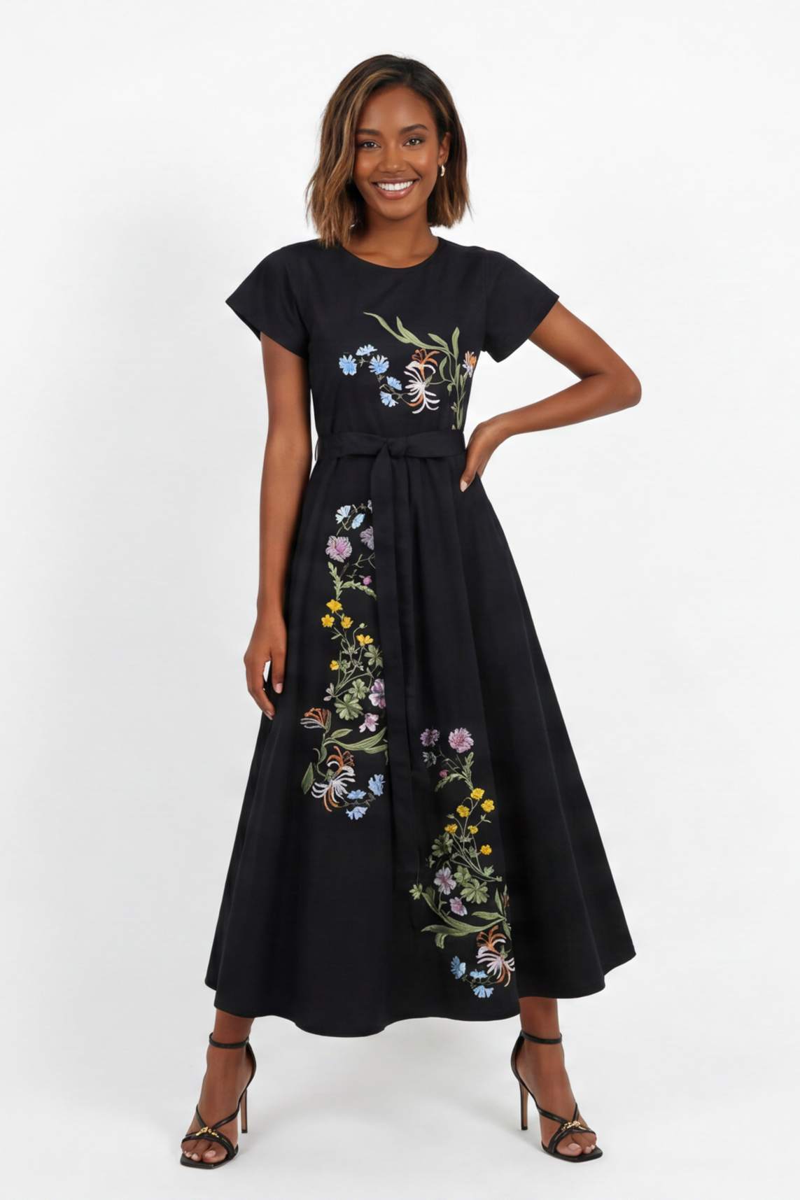 Model wearing embroidered midi dress with asymmetrical floral embroidery, cap sleeves, and removable self-tie waist belt