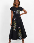 Model wearing embroidered midi dress with asymmetrical floral embroidery, cap sleeves, and removable self-tie waist belt