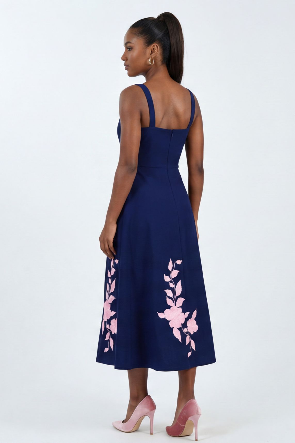 Model wearing the Fanm Mon Elmas Dress featuring oversized hibiscus-inspired embroidery, square back neckline, fitted bodice, and softly flared midi skirt against a neutral studio background.