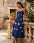 Model wearing the Fanm Mon Fisayo Dress featuring climbing rose embroidery, square neckline, fitted bodice, and elegant midi silhouette styled outdoors in a resort-inspired setting.