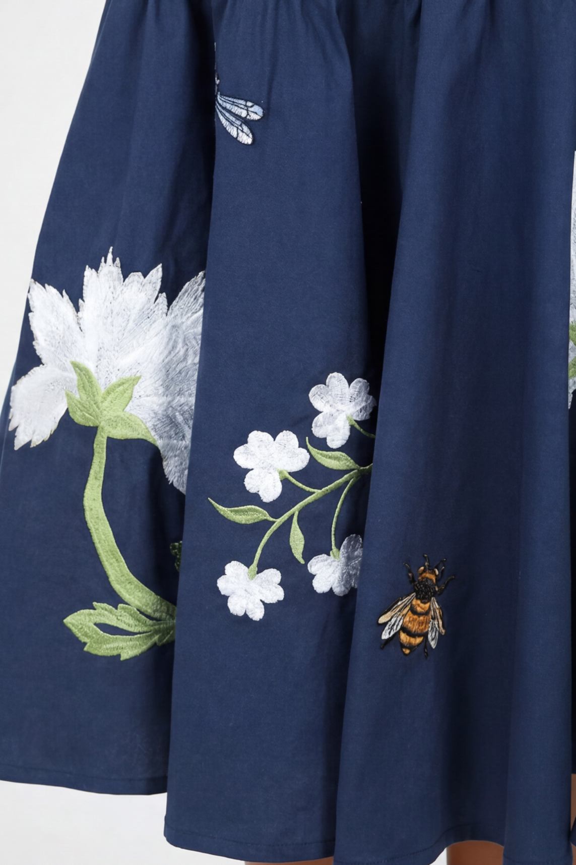 Detailed view of the Fanm Mon Gayelle Dress embroidery featuring cosmos flowers, cherry blossoms, dragonflies, and bee motifs on the flounced midi skirt hem.