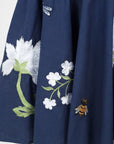 Detailed view of the Fanm Mon Gayelle Dress embroidery featuring cosmos flowers, cherry blossoms, dragonflies, and bee motifs on the flounced midi skirt hem.