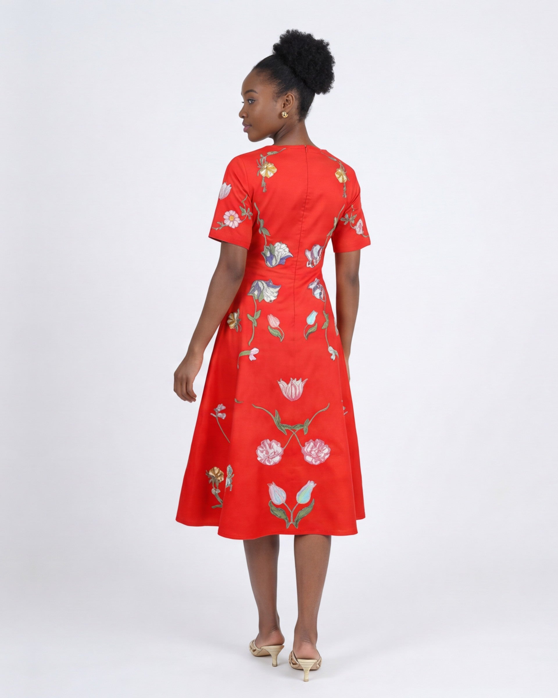 Model wearing the Fanm Mon Hannah Dress featuring tulip and poppy floral embroidery, short sleeves, fitted bodice, and flowing midi skirt in back view against a neutral background.