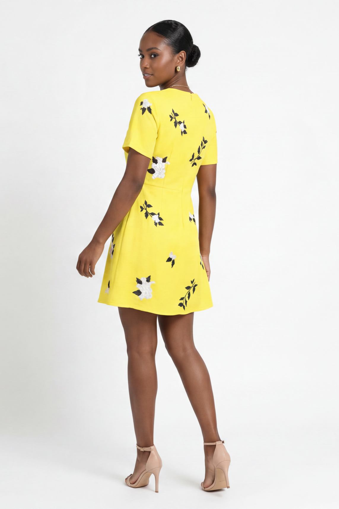 Model wearing the Fanm Mon Hariette Dress with scattered jasmine blossom embroidery, short sleeves, and tailored mini silhouette shown from the back against a neutral  background.