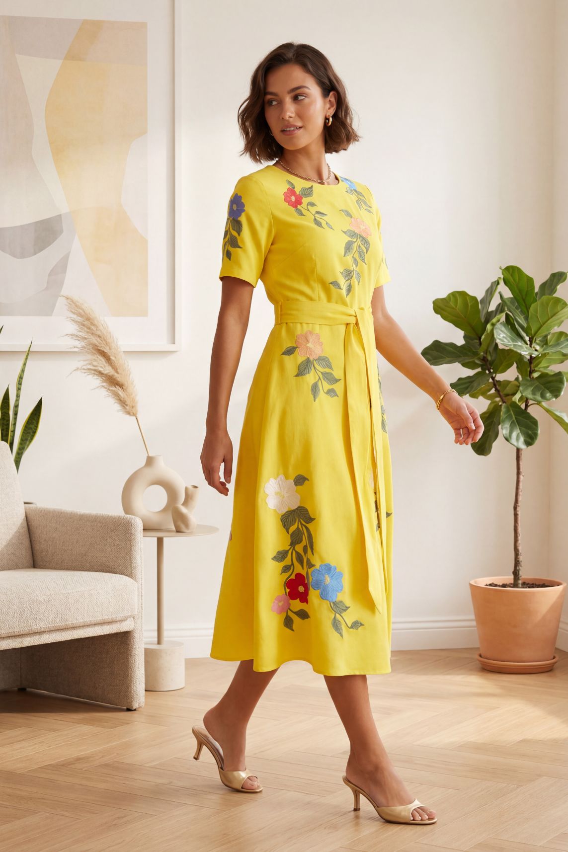 Model wearing Fanm Mon elegant embroidered Jess midi dress with floral blooms and green vine detailing and belted waist styled indoors for occasion and resort wear.
