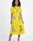 Model wearing Fanm Mon Jess embroidered midi dress with floral botanical motifs, short sleeves, round neckline, and self-tie waist belt against a  off white  background.