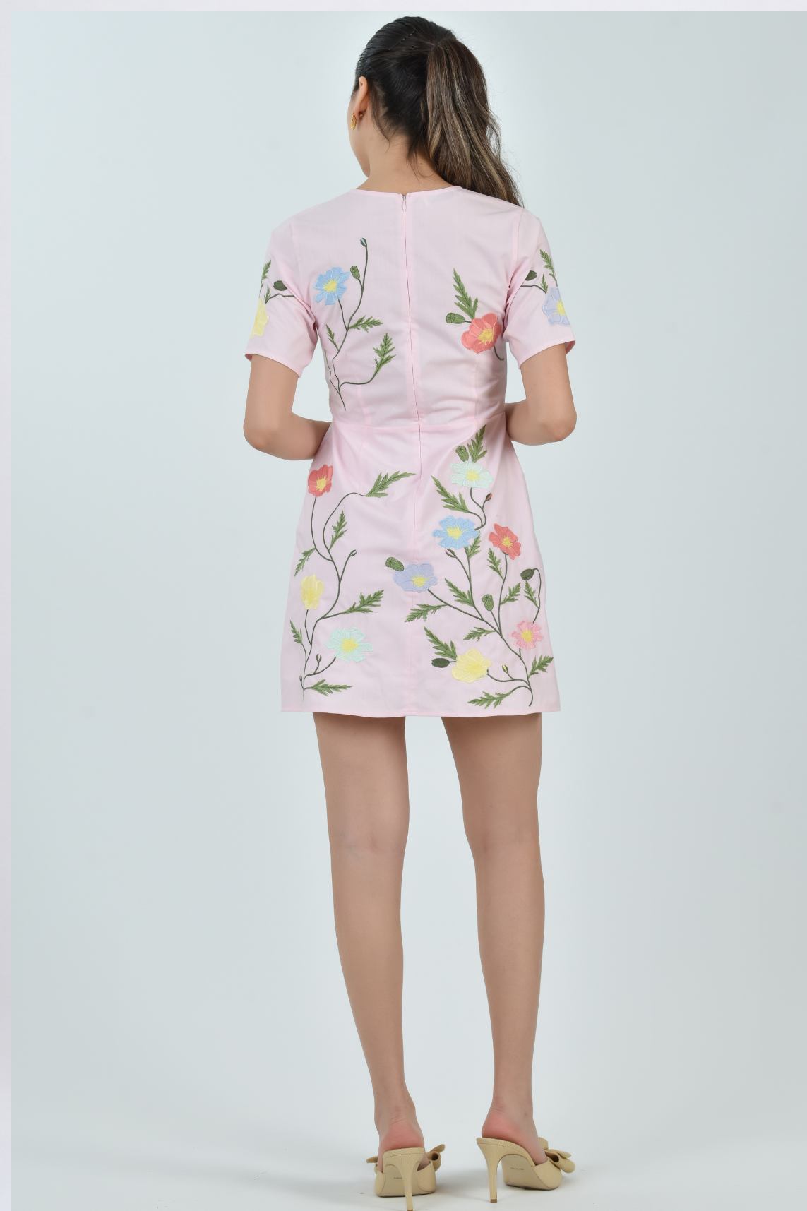 Model wearing the Fanm Mon Light Pink Joe Dress featuring hand-placed cosmos flower, poppy, and buttercup embroidery on a tailored mini silhouette against a neutral  background.