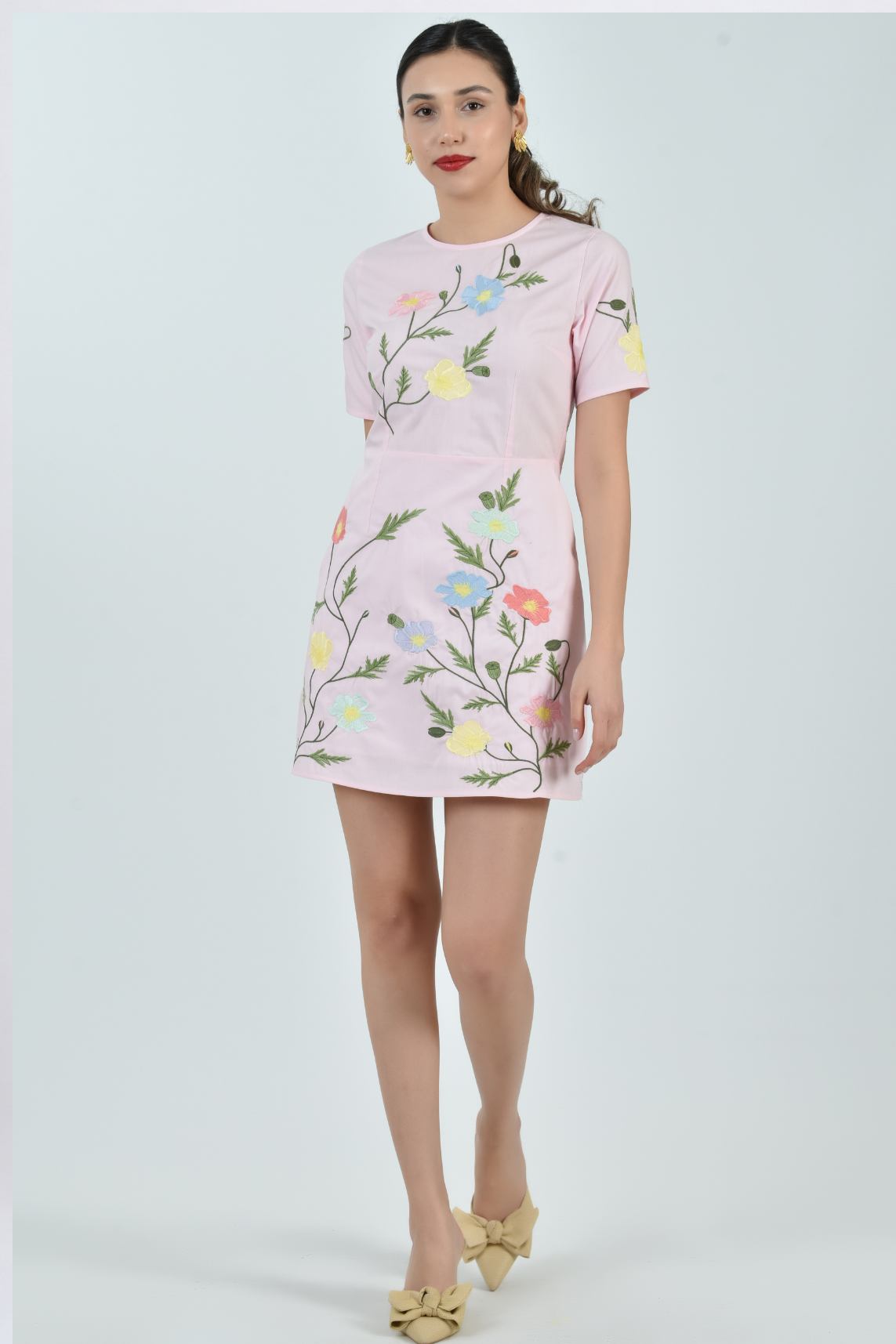 Model wearing the Fanm Mon Joe Dress  in Light Pink Poplin cotton featuring hand-placed cosmos flower, poppy, and buttercup embroidery on a tailored mini silhouette against a neutral studio background.