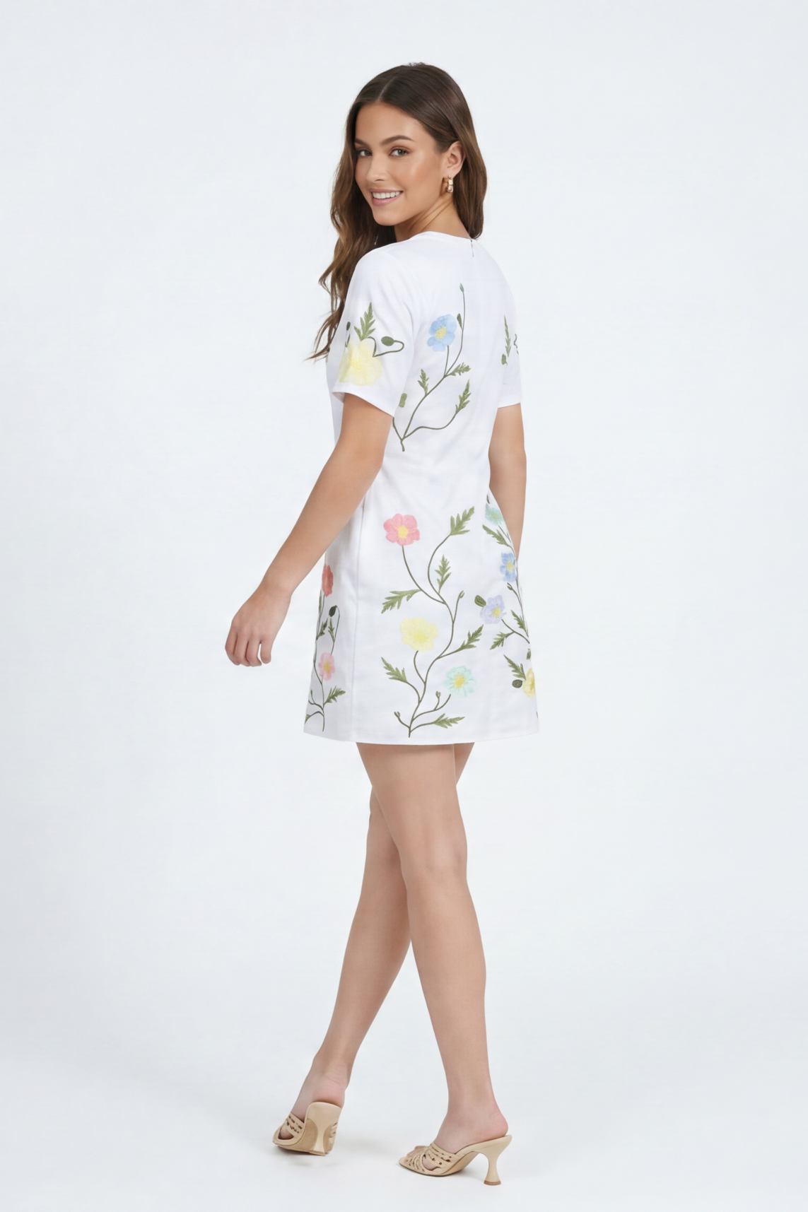 Model wearing the Fanm Mon Joe Dress in White with trailing wildflower embroidery, short sleeves, and tailored mini silhouette shown from the back against an off white background.