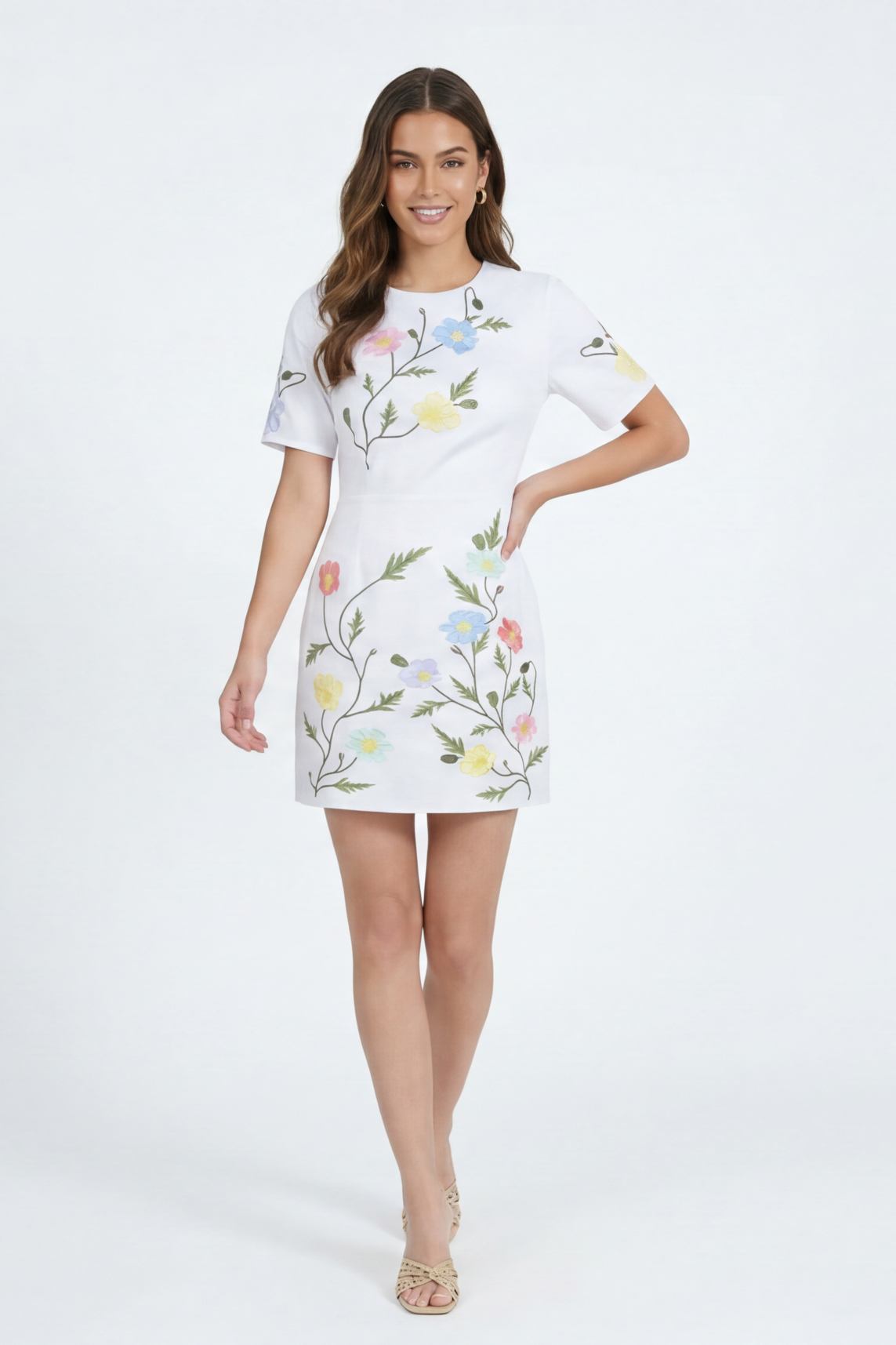 Model wearing the Fanm Mon Joe Dress in White featuring hand-placed wild poppy, cosmos, and buttercup embroidery on a tailored short sleeve mini silhouette against an off-white background.