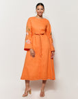 Fanm Mon Long Sleeve Cotton Lagos Dress Shown on Model in Orange, front view of dress with bell sleeves and waist tie. 