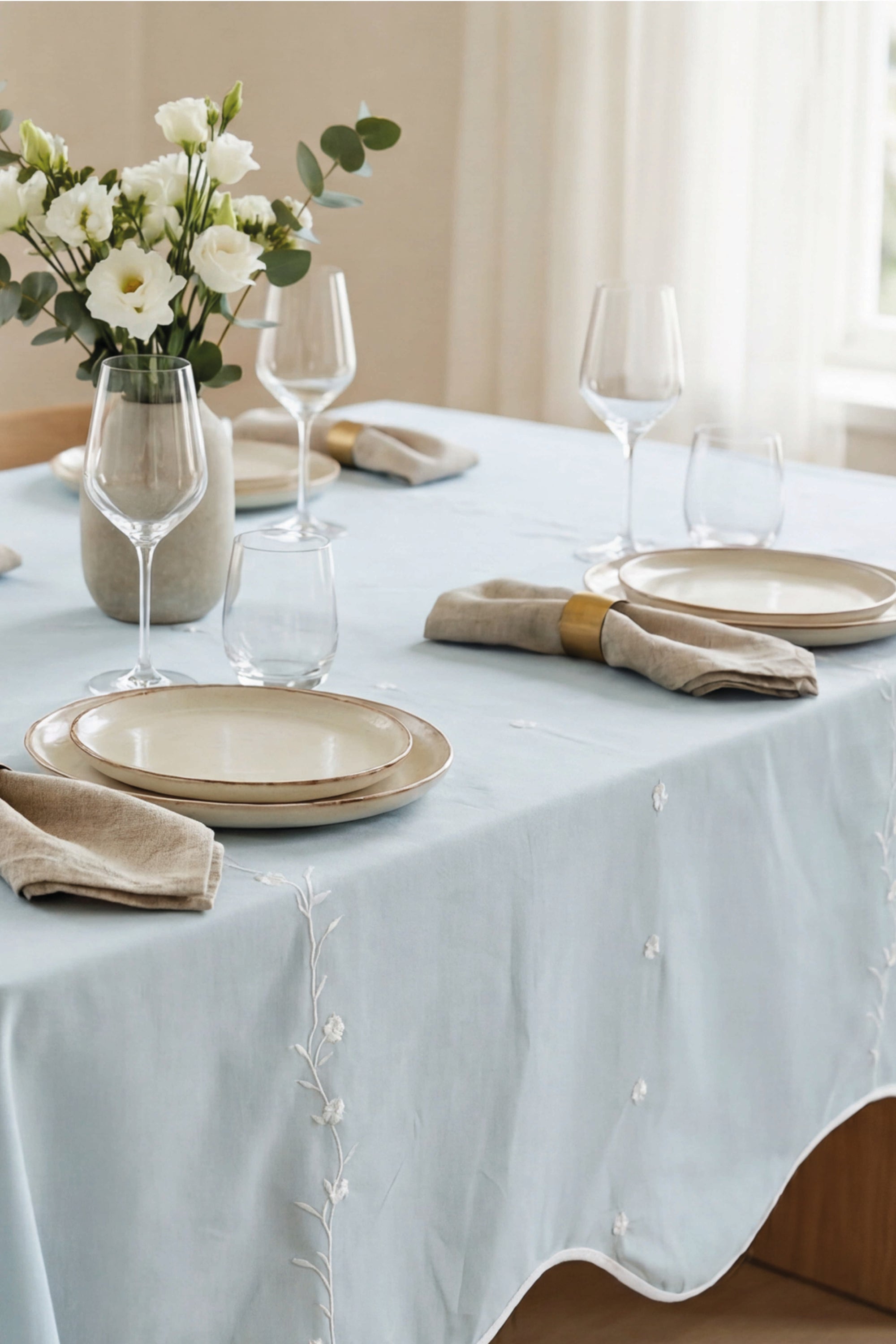 Elegant table setting with light lagoon tablecloth, white flowers, and beige plates.